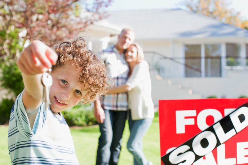 Family-in-front-of-sold-sign-with-kid-holding-house-keys